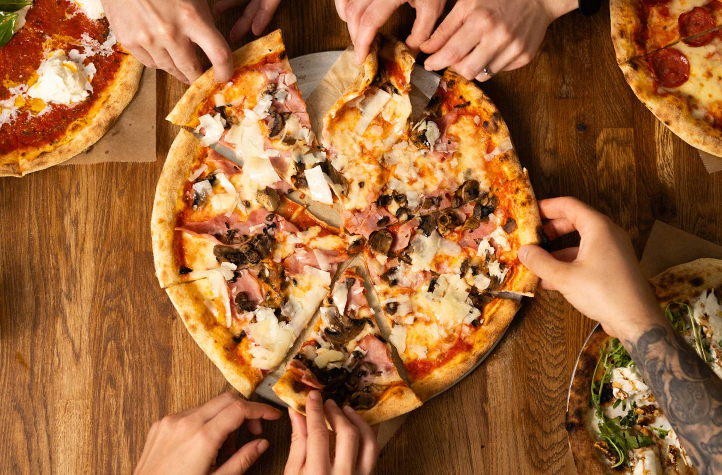 Multiple people grabbing at slides of a Hawaiian pizza